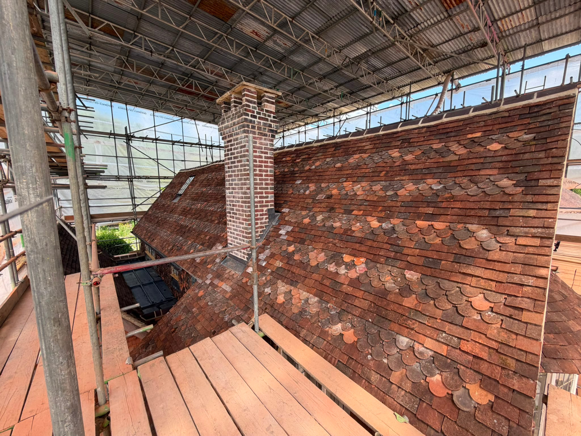 Clay tiles being laid on a steep roof slope around a brick chimney with new lead flashing