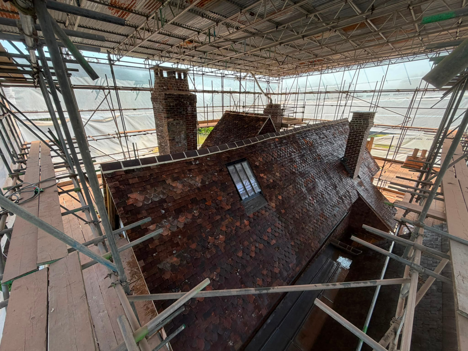 Restored clay tiled roof across several levels with brick chimneys and lead valleys