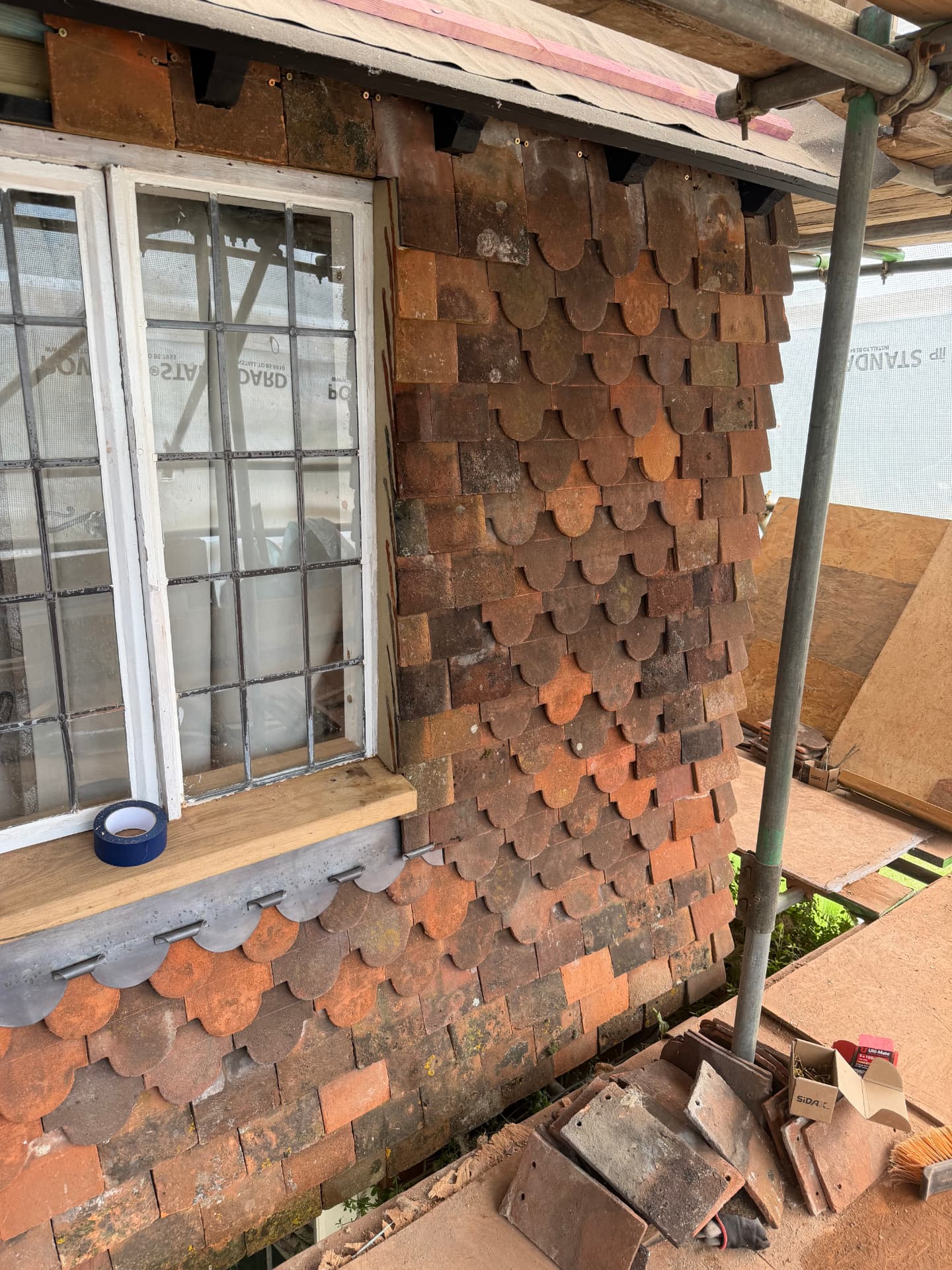 Handmade clay tiles hung vertically on a wall beside a leaded-light window